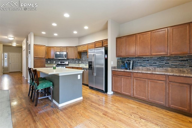 kitchen with appliances with stainless steel finishes, light hardwood / wood-style floors, tasteful backsplash, and a breakfast bar area