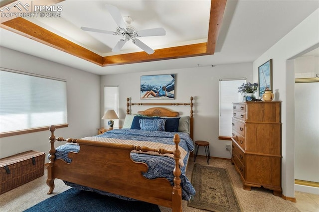 carpeted bedroom with multiple windows, a tray ceiling, and ceiling fan