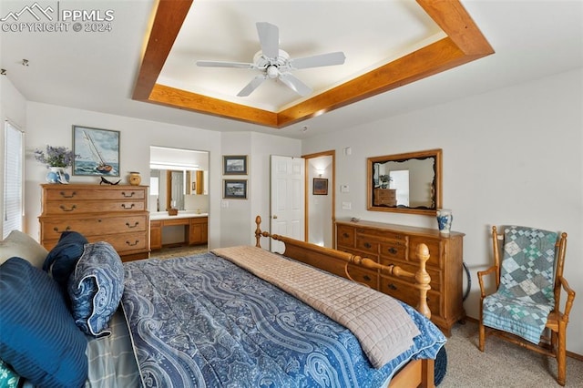 bedroom with a raised ceiling, connected bathroom, ceiling fan, and carpet