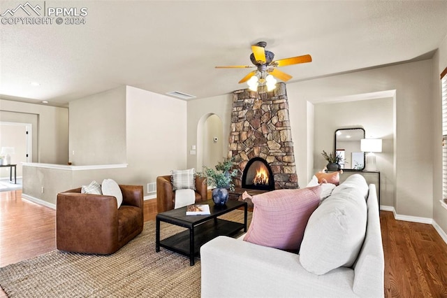 living room with wood-type flooring, a stone fireplace, and ceiling fan