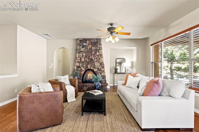 living room featuring wood-type flooring, a stone fireplace, and ceiling fan