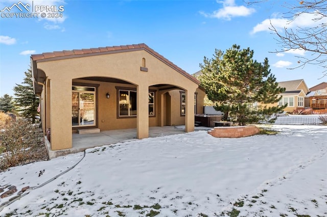 snow covered property with a patio and a hot tub