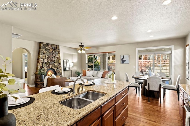 kitchen with sink, light stone counters, a textured ceiling, a fireplace, and hardwood / wood-style flooring