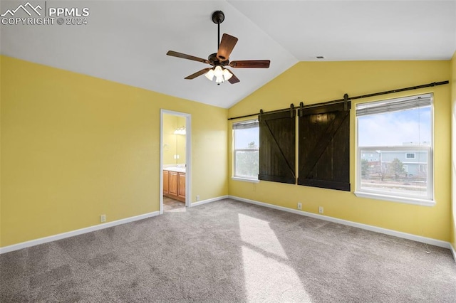 carpeted spare room with ceiling fan, a barn door, and vaulted ceiling