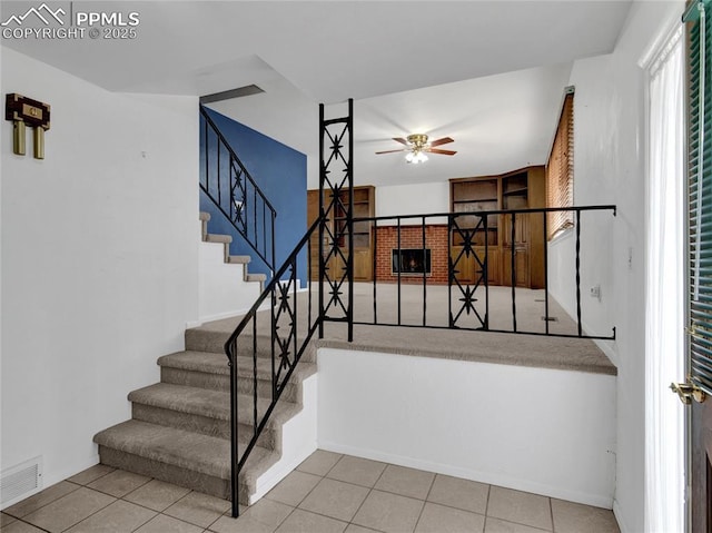 stairway with ceiling fan, tile patterned flooring, and a brick fireplace