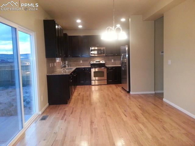 kitchen featuring hanging light fixtures, stainless steel appliances, light hardwood / wood-style flooring, a notable chandelier, and backsplash