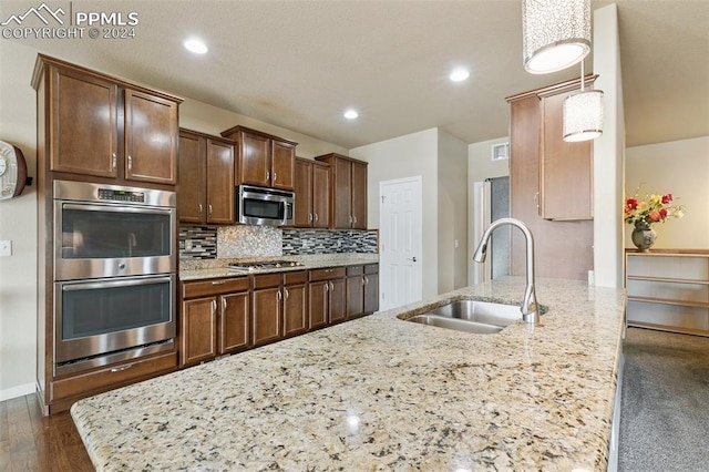 kitchen with light stone counters, sink, stainless steel appliances, and decorative light fixtures