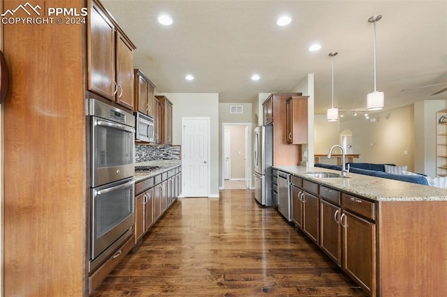 kitchen featuring dark wood-type flooring, sink, hanging light fixtures, light stone counters, and stainless steel appliances