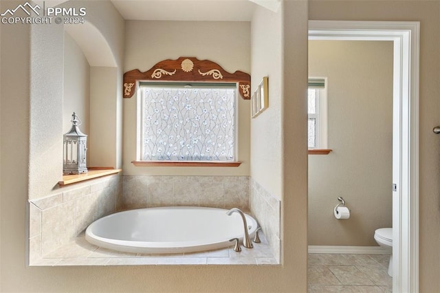 bathroom featuring tile patterned flooring, toilet, and tiled tub