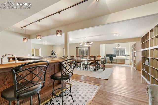 bar with rail lighting, a textured ceiling, sink, decorative light fixtures, and light hardwood / wood-style flooring