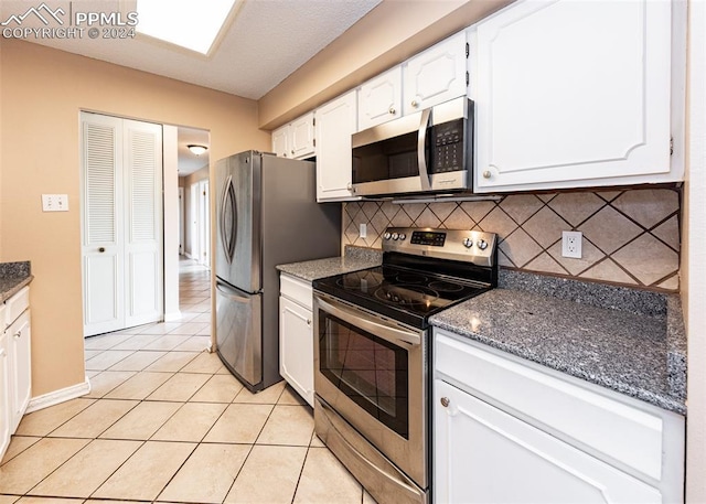 kitchen featuring decorative backsplash, dark stone countertops, light tile patterned floors, white cabinetry, and stainless steel appliances