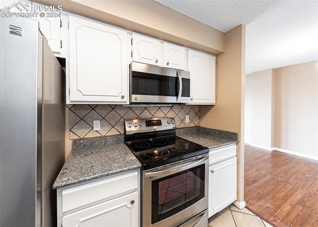 kitchen featuring white cabinetry, backsplash, a textured ceiling, appliances with stainless steel finishes, and light wood-type flooring