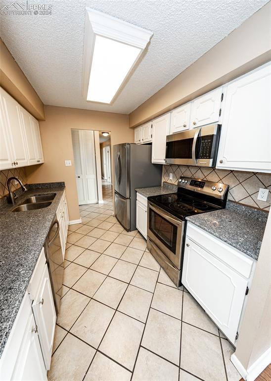 kitchen featuring white cabinets, sink, decorative backsplash, light tile patterned flooring, and stainless steel appliances