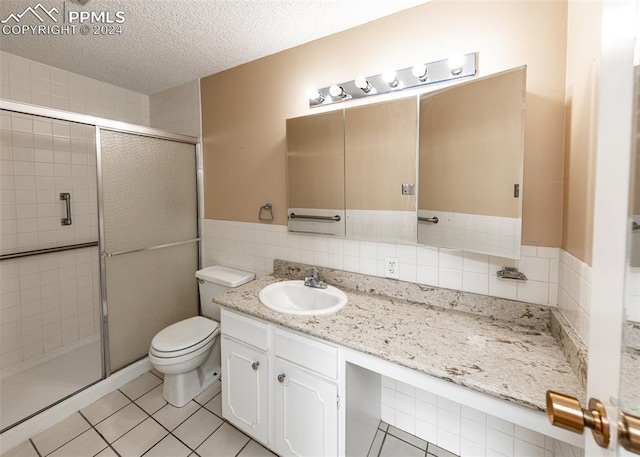 bathroom featuring tile patterned floors, a textured ceiling, toilet, a shower with door, and vanity