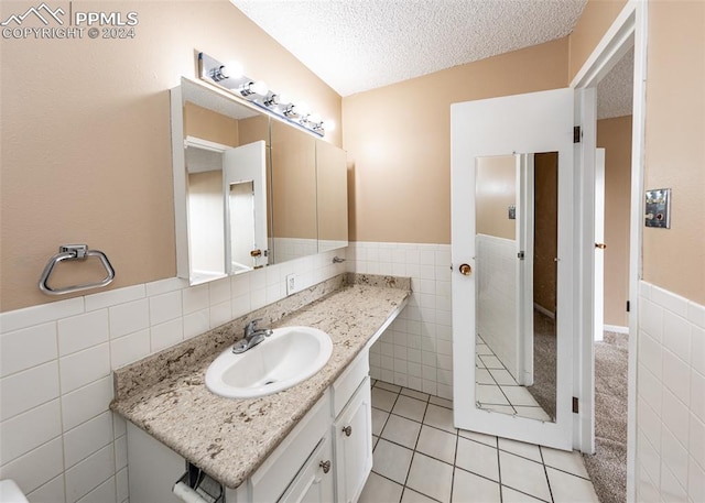 bathroom with tile walls, tile patterned flooring, vanity, and a textured ceiling