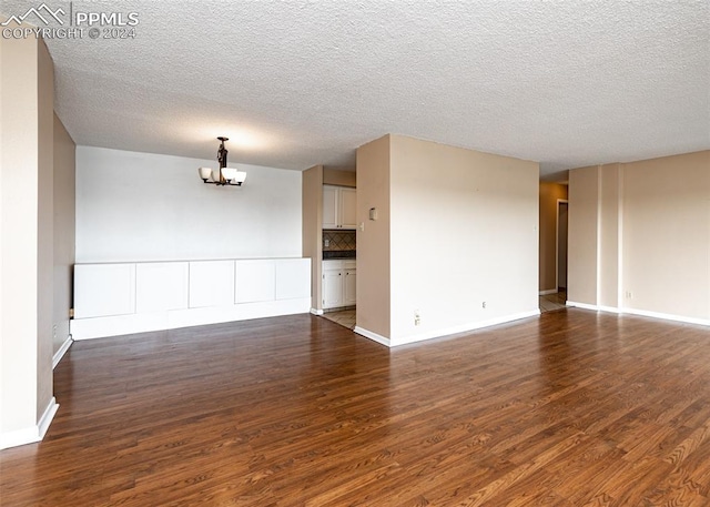 empty room with a notable chandelier, dark hardwood / wood-style flooring, and a textured ceiling