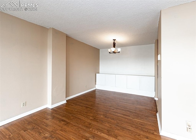 unfurnished room featuring a textured ceiling, dark hardwood / wood-style flooring, and an inviting chandelier