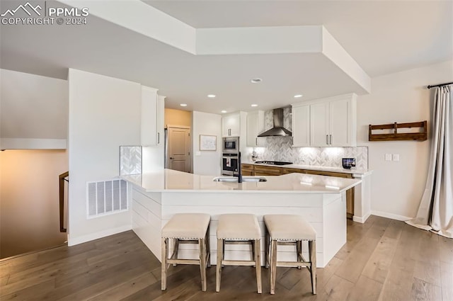 kitchen featuring kitchen peninsula, wall chimney exhaust hood, white cabinets, dark hardwood / wood-style floors, and stainless steel microwave