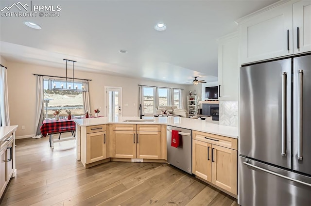 kitchen featuring sink, hanging light fixtures, light hardwood / wood-style flooring, stainless steel appliances, and a tiled fireplace