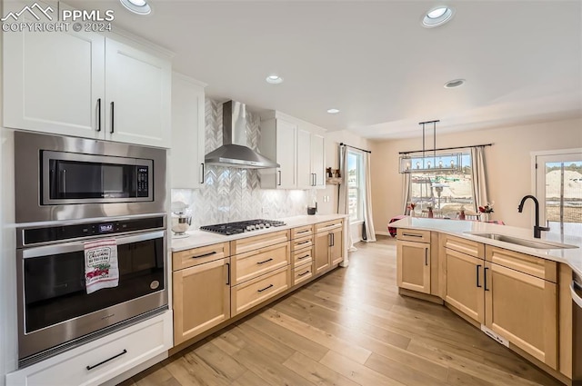 kitchen featuring sink, wall chimney exhaust hood, light hardwood / wood-style flooring, decorative light fixtures, and appliances with stainless steel finishes