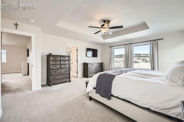 bedroom with ceiling fan, a raised ceiling, ensuite bathroom, and light carpet