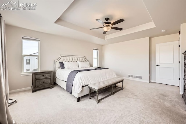 carpeted bedroom featuring ceiling fan, a raised ceiling, and multiple windows