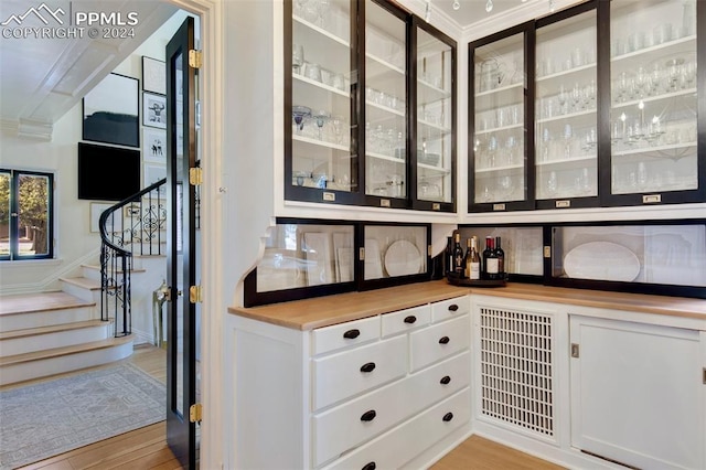 bar with light hardwood / wood-style floors, white cabinetry, and crown molding