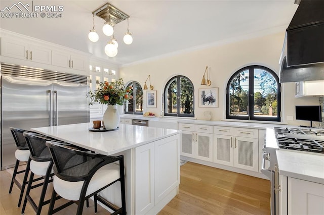 kitchen with light hardwood / wood-style flooring, crown molding, decorative light fixtures, white cabinets, and appliances with stainless steel finishes