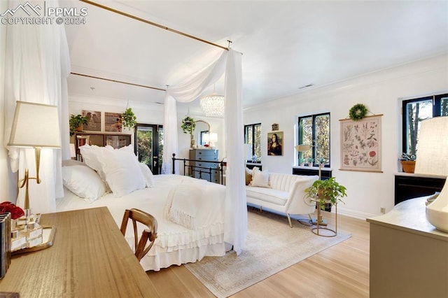 bedroom featuring a chandelier, light hardwood / wood-style floors, ornamental molding, and multiple windows