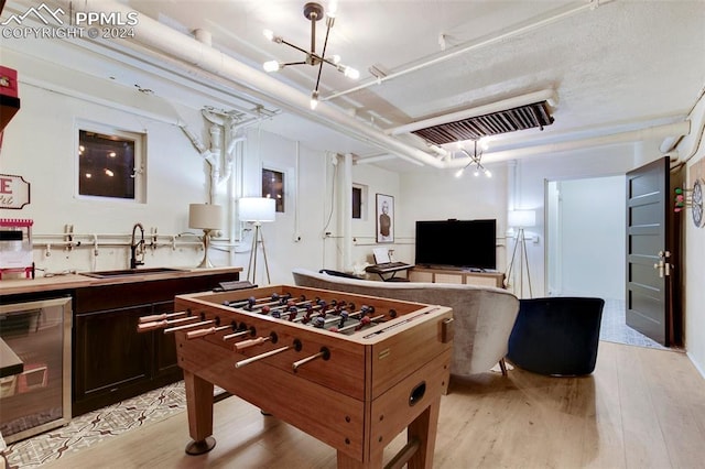 recreation room with light wood-type flooring, sink, beverage cooler, and a chandelier