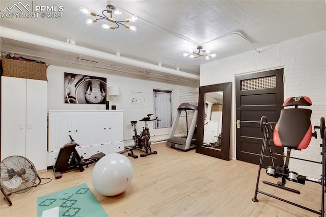 workout area with hardwood / wood-style flooring, brick wall, and an inviting chandelier