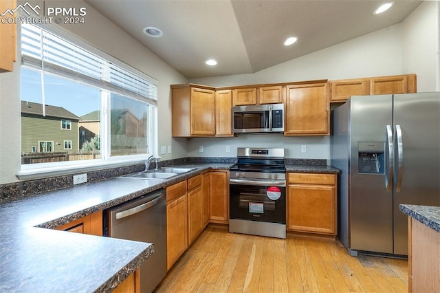 kitchen featuring appliances with stainless steel finishes, light wood-type flooring, vaulted ceiling, and sink