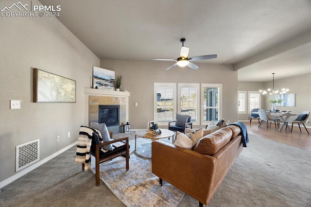 carpeted living room with ceiling fan with notable chandelier and a tiled fireplace