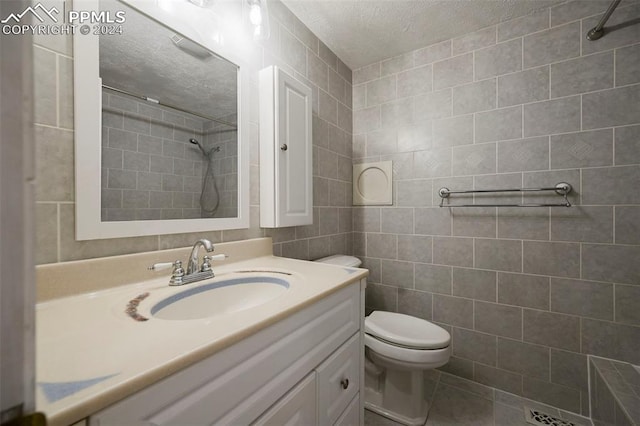 bathroom with a tile shower, vanity, a textured ceiling, tile walls, and toilet