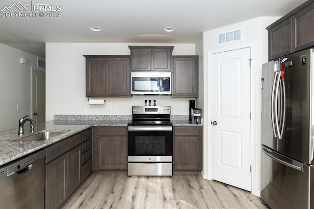 kitchen featuring light stone countertops, appliances with stainless steel finishes, kitchen peninsula, sink, and light hardwood / wood-style flooring