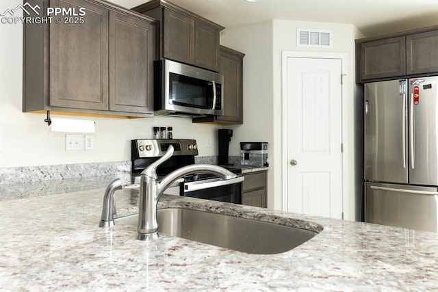 kitchen featuring light stone countertops, dark brown cabinets, sink, and appliances with stainless steel finishes