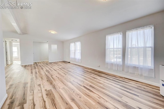 unfurnished living room with beam ceiling and light wood-type flooring