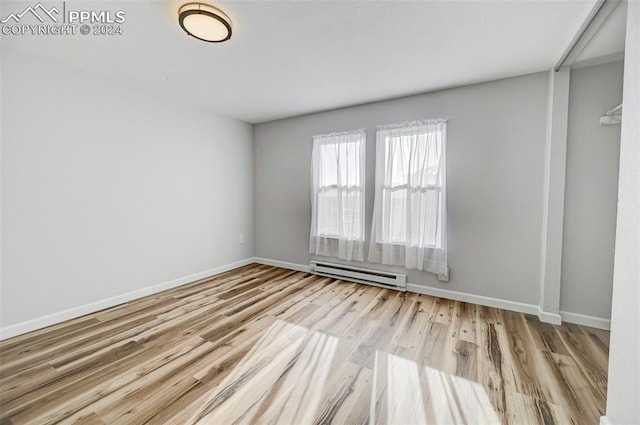 spare room featuring a baseboard heating unit and light wood-type flooring