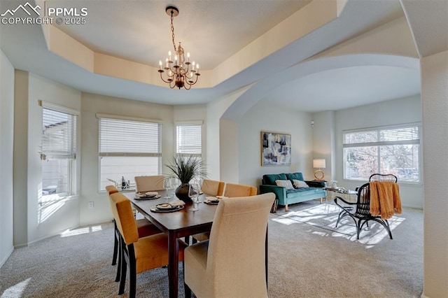 carpeted dining space with an inviting chandelier and a tray ceiling