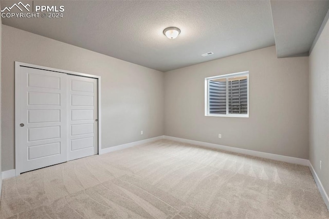 unfurnished bedroom featuring light colored carpet, a textured ceiling, and a closet