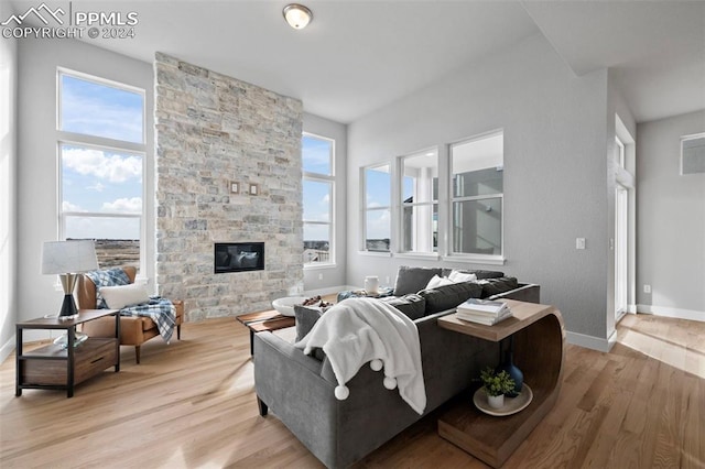 living room with a stone fireplace, a healthy amount of sunlight, and light wood-type flooring