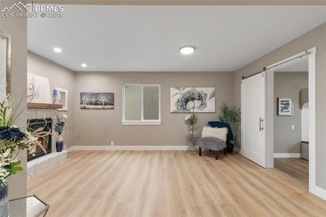 sitting room with light wood-type flooring, a barn door, and a fireplace