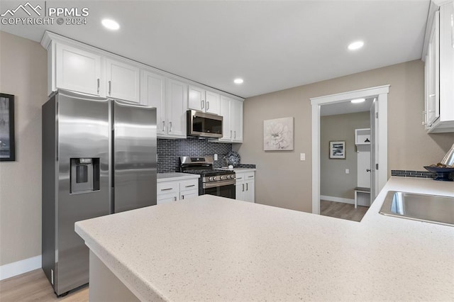 kitchen featuring light hardwood / wood-style flooring, decorative backsplash, white cabinetry, kitchen peninsula, and stainless steel appliances