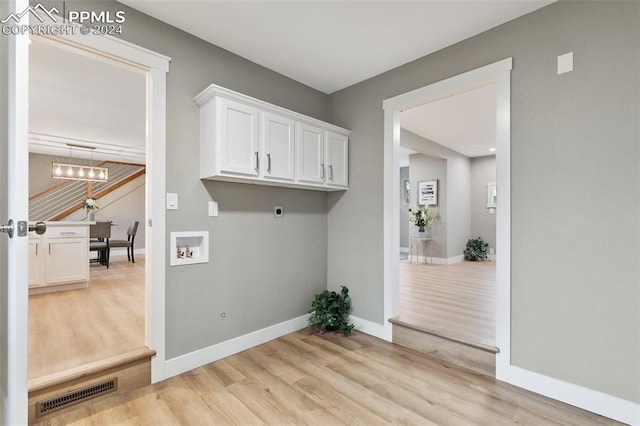 clothes washing area with electric dryer hookup, cabinets, a chandelier, and light hardwood / wood-style flooring