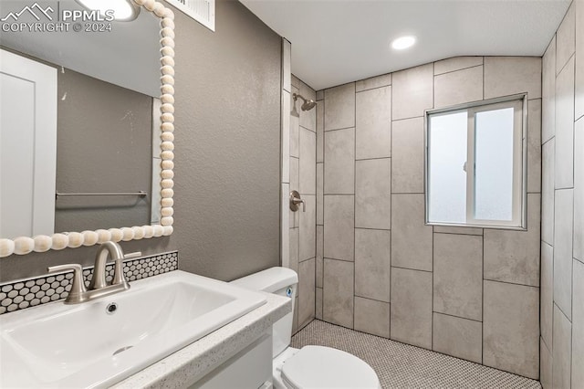 bathroom with vanity, toilet, lofted ceiling, and tiled shower