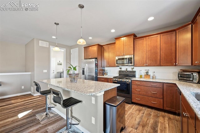 kitchen with light stone countertops, hanging light fixtures, stainless steel appliances, wood-type flooring, and a breakfast bar