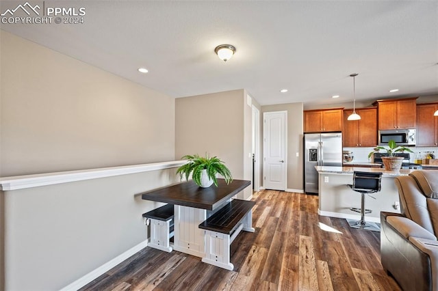 kitchen with a kitchen breakfast bar, dark hardwood / wood-style flooring, pendant lighting, and appliances with stainless steel finishes