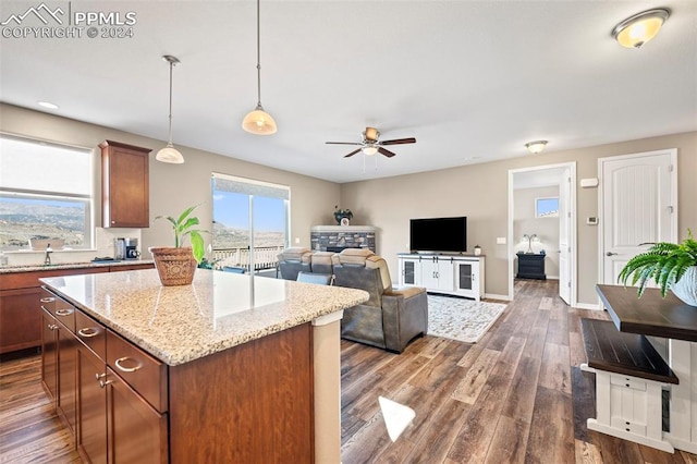 kitchen featuring light stone countertops, ceiling fan, dark wood-type flooring, a kitchen island, and hanging light fixtures