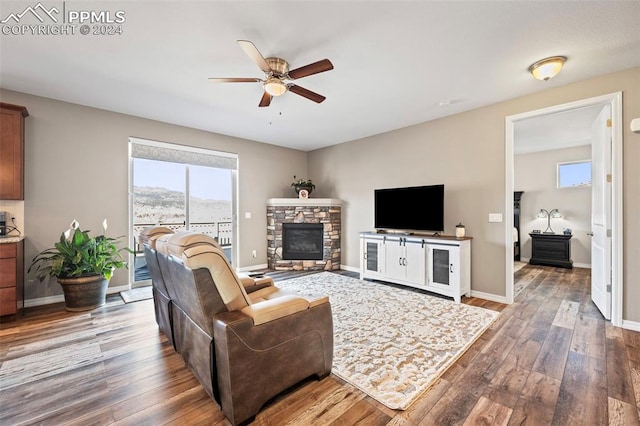 living room with ceiling fan, a stone fireplace, and dark wood-type flooring