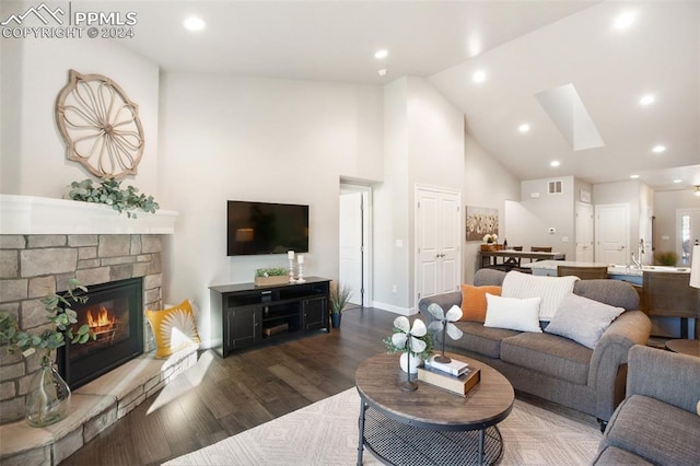 living room with a stone fireplace, dark wood-type flooring, high vaulted ceiling, and a skylight